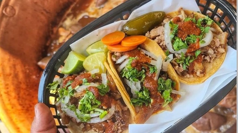 a tray of 3 tacos held over a pot of carnitas cooking
