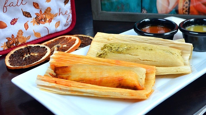 2 tamales on a table surrounded by sauce and sliced citrus