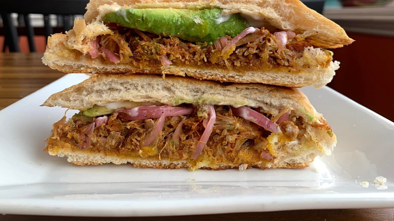close-up of a torta cut in half and stacked to show a filling of meat, red onion, and avocado