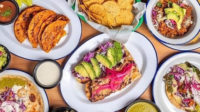 overhead shot of a table full of plated dishes from Tlaolli, including tacos and an open-faced torta
