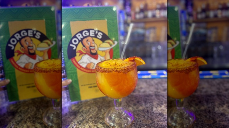 a colorful blended margarita with a hand holding the Jorge's menu behind it