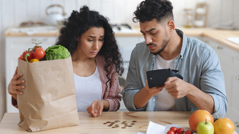 Couple with groceries counting coins at kitchen table