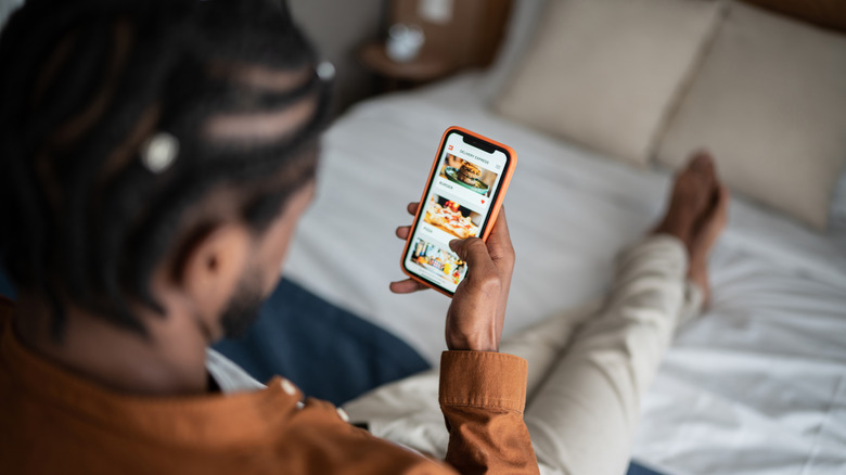 Man using grocery app on smartphone in bed