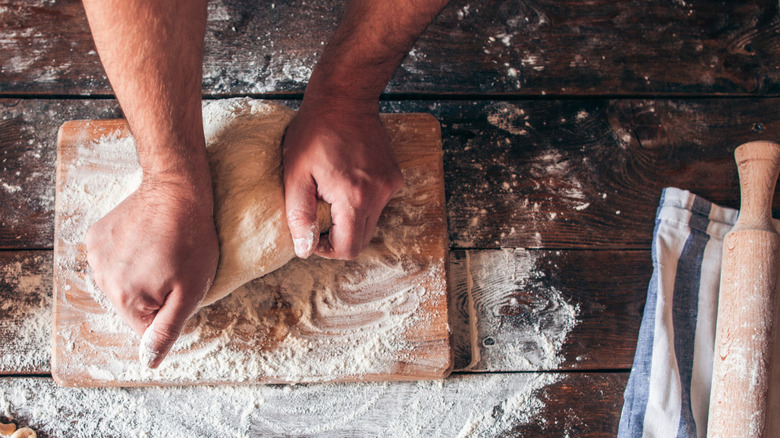 Hands stretching dough on floured work surface