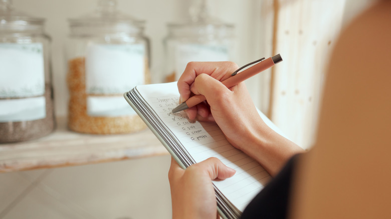 Woman writing grocery list while looking in pantry