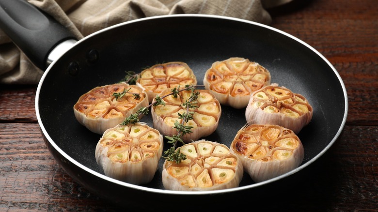 Grilled garlic with thyme in frying pan on wooden table