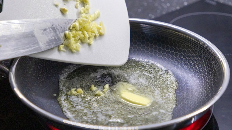 Person adding minced garlic to melted butter in a frying pan on a hot stovetop