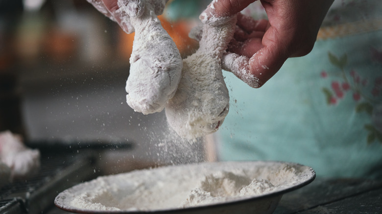 Two chicken drumsticks being caked in flour