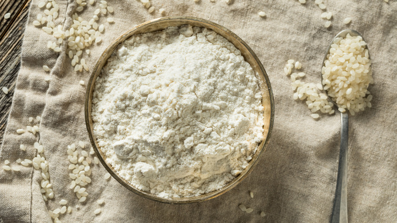 Rice flour in a bowl with grains of rice surrounding it.