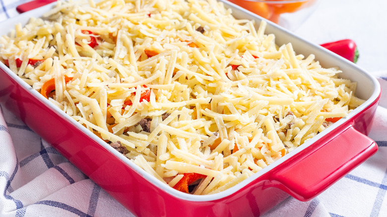 An uncooked casserole with a cheese topping.