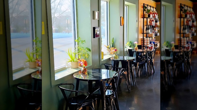 Three round tables next to window with a shelf on wine bottles in the background at Solely Wine