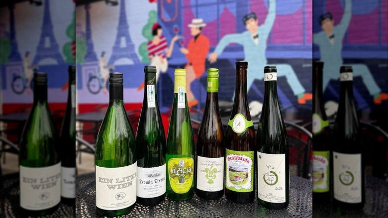 Six bottles of wine on an outdoor table with a French-inspired mural in the background