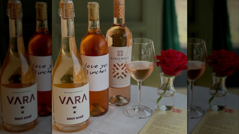Three bottles of rosé wine, a glass of rosé wine, and a single rose in a small vase