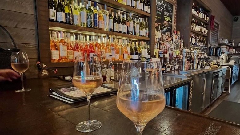 Glasses of wine with bottles of wine shelved behind the bar at Mary Kate's Wine Bar
