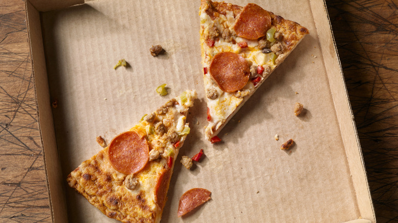 Two slices of cold pizza with pepperoni and sausage in a cardboard pizza box