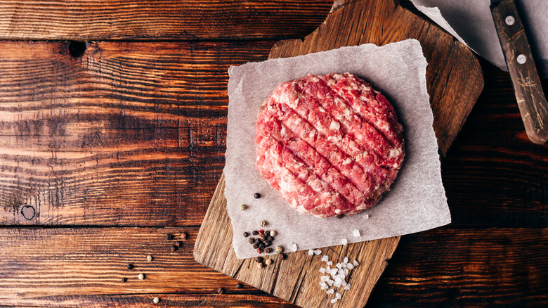 A raw beef patty that looks home made shot from above and sitting on a cutting board