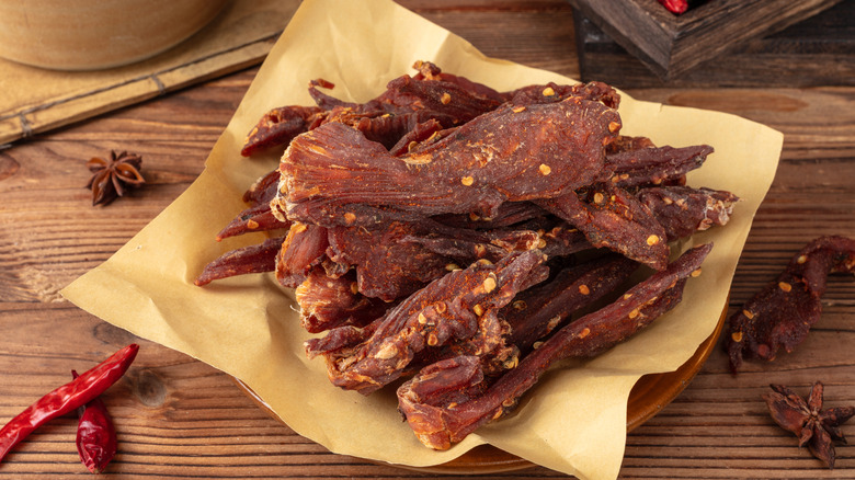 Homemade chicken jerky stacked on paper on a wooden table