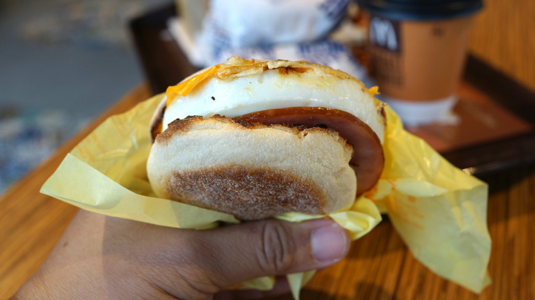 A hand holds an Egg McMuffin that has been partially unwrapped.