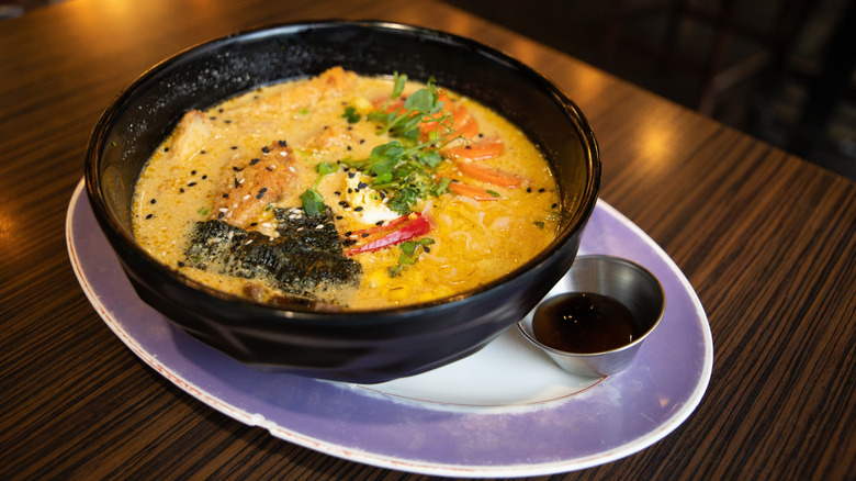 Freshly cooked Japanese ramen with chicken, mushrooms, eggs and bok choy cabbage served in a bowl and extra sauce on the side.