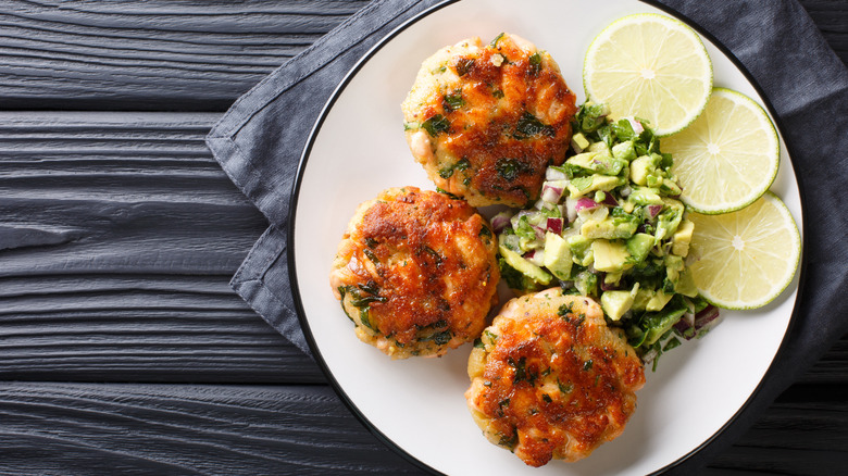 A top down view of salmon cakes on a plate with lime and avocado salad