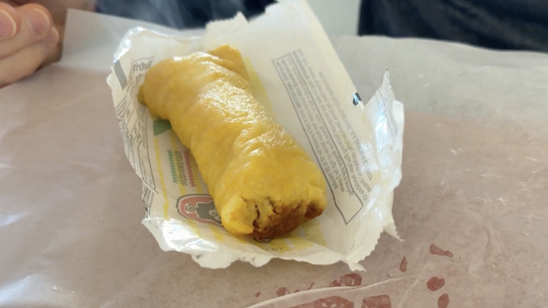 A Supreme tamale sitting in a partially opened paper wrapper.