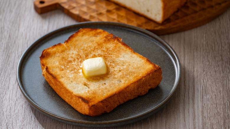 A large pat of butter melts on a piece of toast on a plate