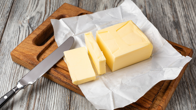 An open package of butter sits on a wooden board with a knife
