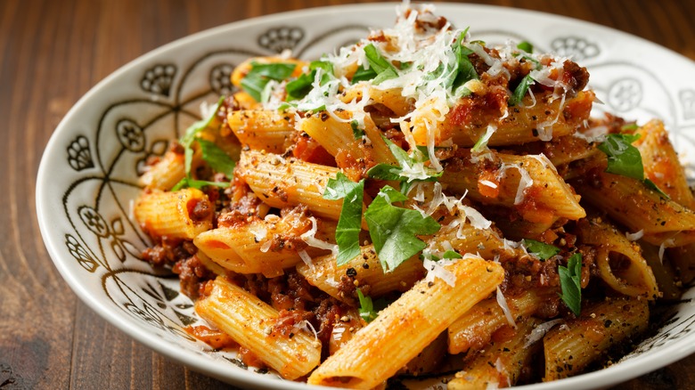 Close up of a bowl of penne bolognese on a wooden table.