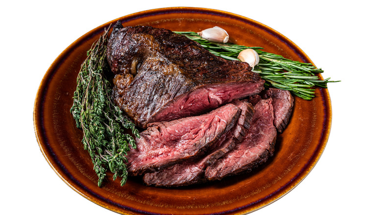 A brown plate with grilled hanger steak on it.