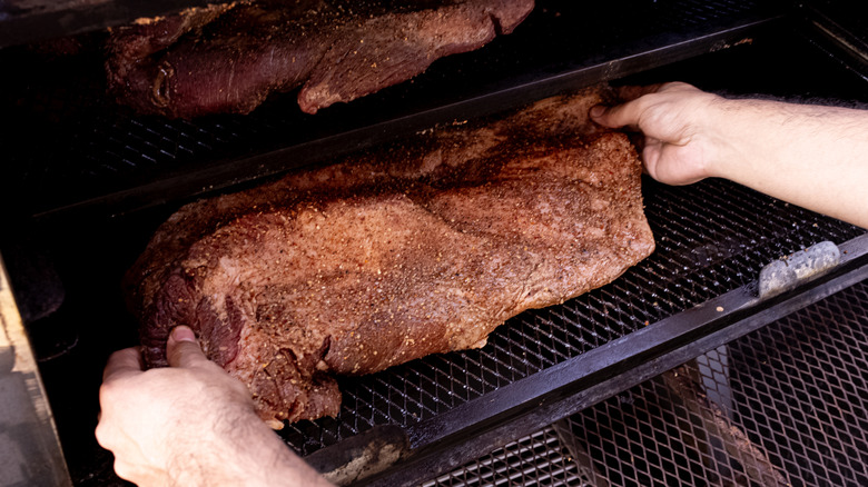 hands putting meat in smoker