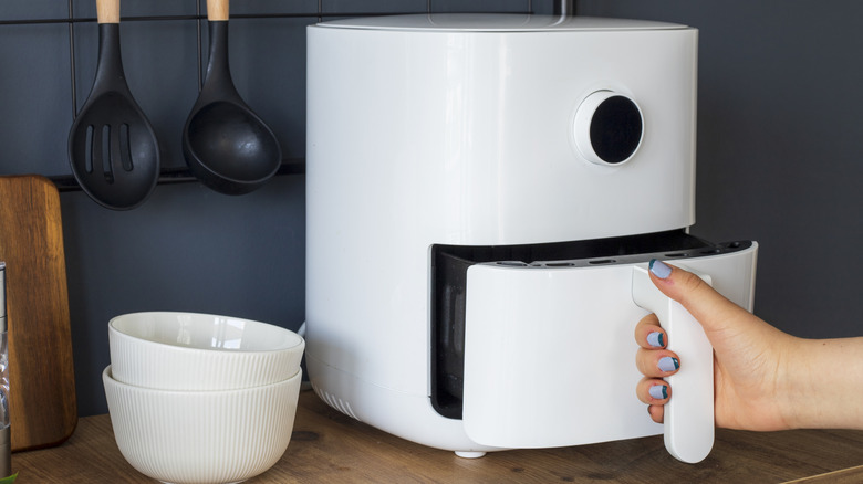 Hands holding onto the handle of a small air fryer basket next to two stacked bowls