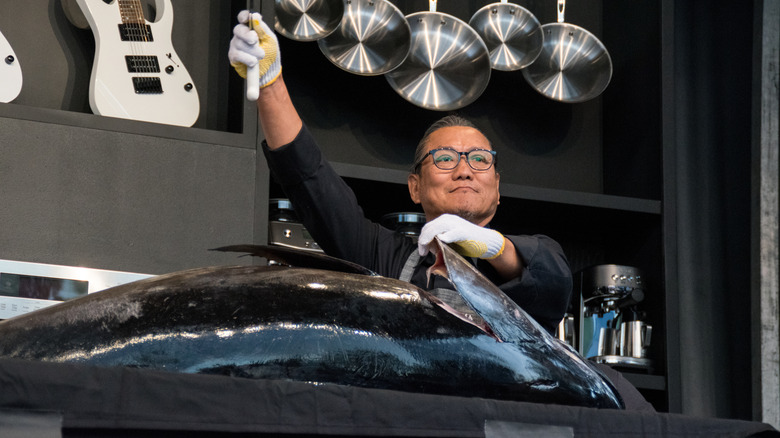 Masaharu Morimoto holding knife up in front of large fish