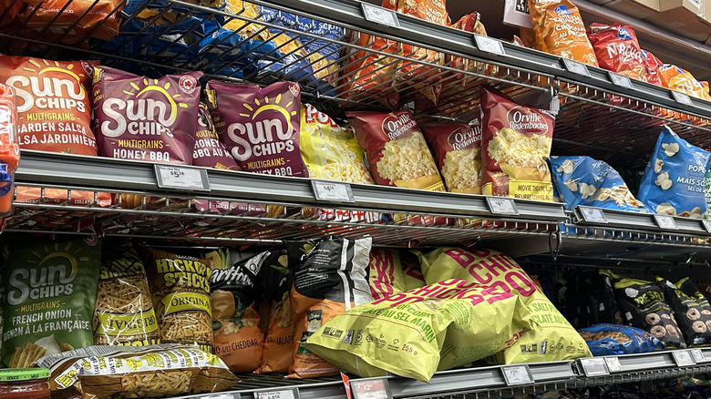 Grocery store shelves stocked with name brand chip and popcorn products.