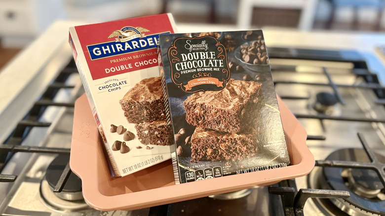 Boxes of Aldi Specially Selected Double Chocolate Premium Brownie Mix and Ghirardelli Double Chocolate Premium Brownie Mix rest on a stovetop