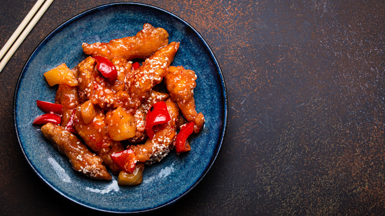 A blue plate of crispy battered chicken tenders in sweet and sour sauce