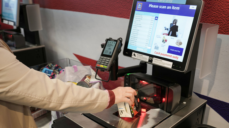 Shopper's hand scanning grocery item at Aldi self-checkout