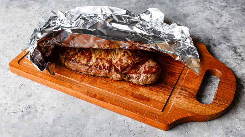 Grilled steak on cutting board covered in aluminum foil