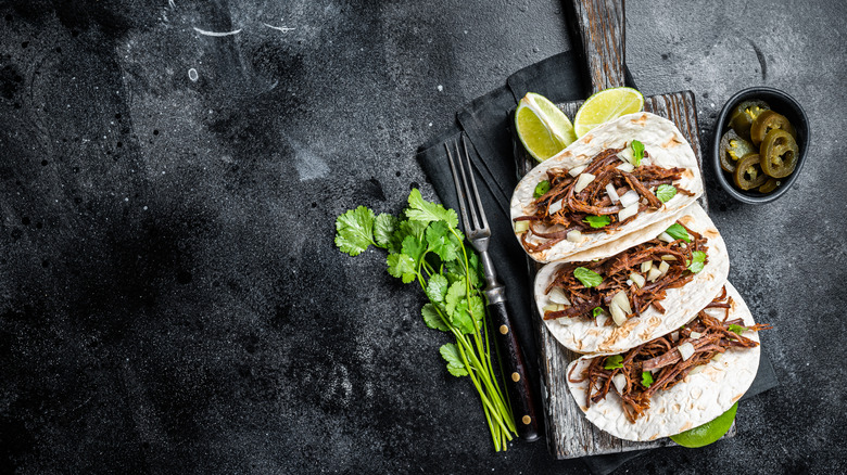 barbacoa tacos lined up on a wooden cutting board
