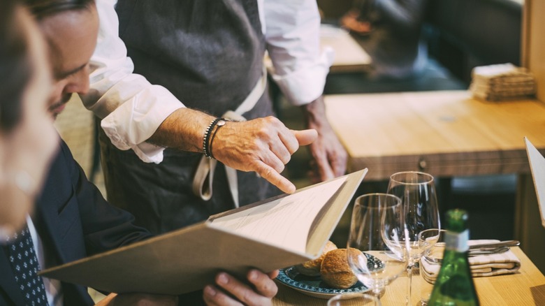 Waiter pointing to restaurant menu in front of guests