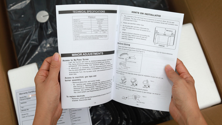 Hands holding an open user manual over a box of new product