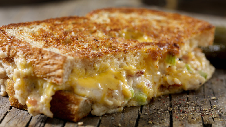 close up of grilled cheese cut in half with cheese oozing out with specks of light green and brown