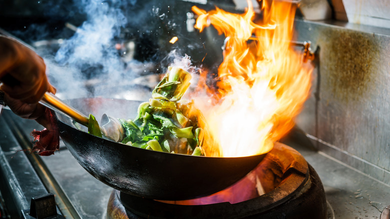 A restaurant chef cooks vegetables in a flaming pan