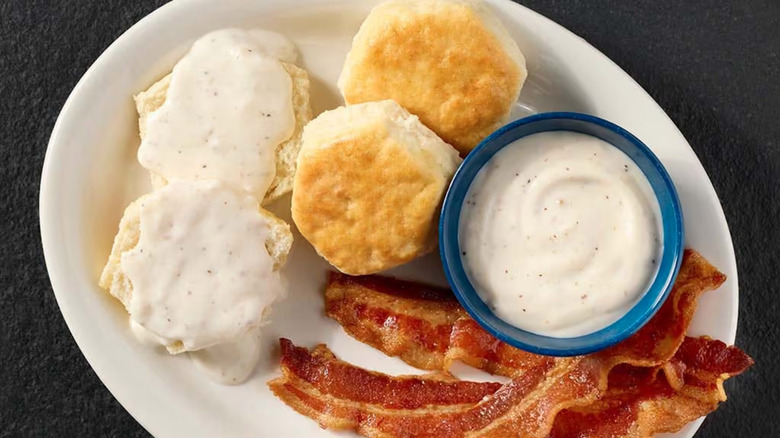 Plate of Cracker Barrel biscuits and gravy with strips of bacon