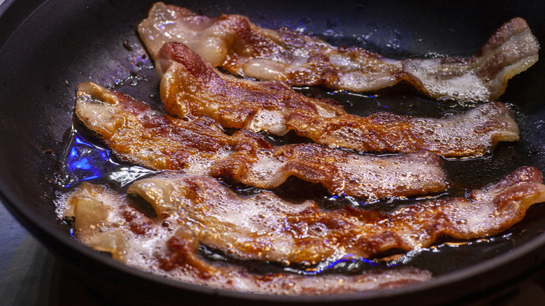 Bacon strips cooking in a frying pan
