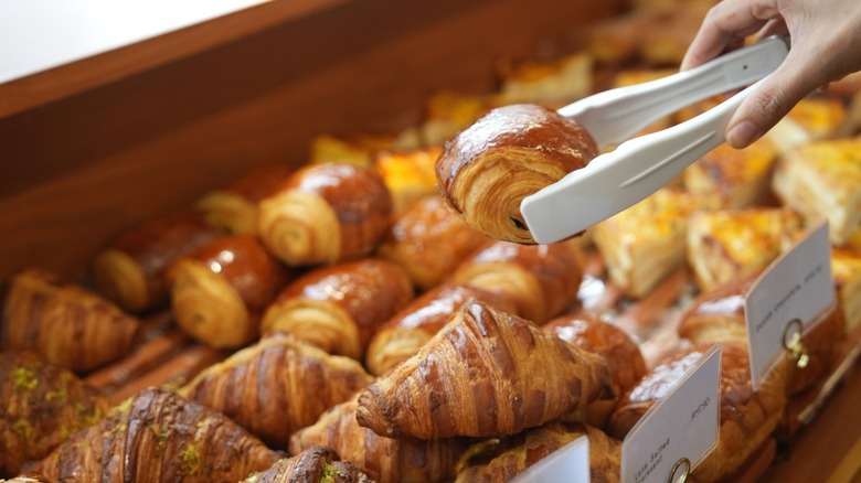 Hand grabbing a pastry with a pair of tongs from a selection of baked goods