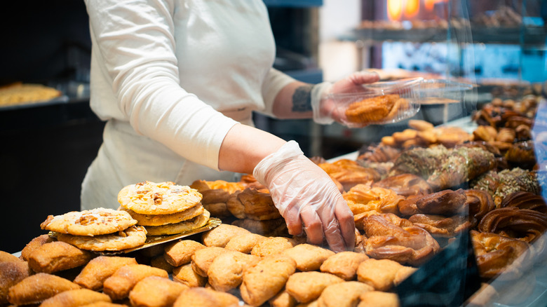 An employee picks up bakery items from the display case at a bakery.