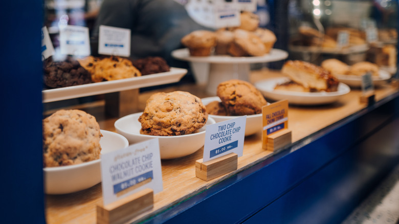 Close-up of Levain bakery cookies in bakery case with other baked-goods blurred in the background.