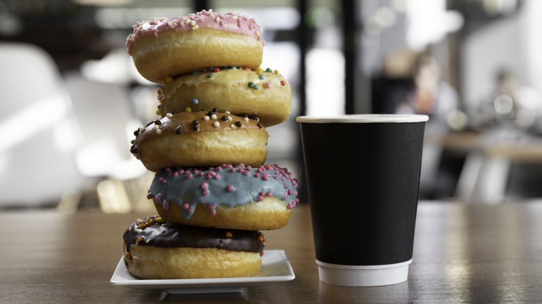 Stack of colorful donuts next to a to-go cup of coffee
