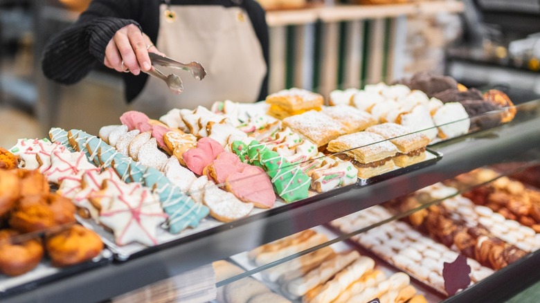 Bakery display with various confections and a worker picking one up with tongs.