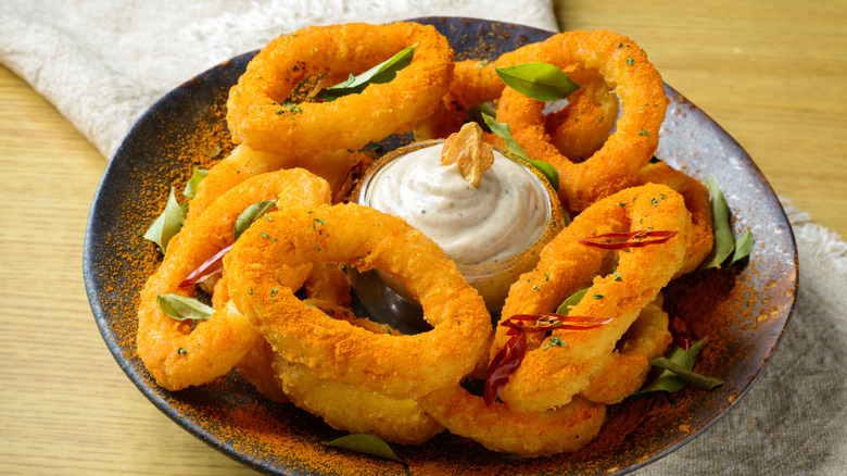 Golden onion rings with spicy seasoning on a rustic plate